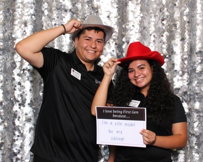 Two UGA students pose in a photo booth. One holds a sign that reads, "I love being first-gen because...I'm a role model for my siblings."